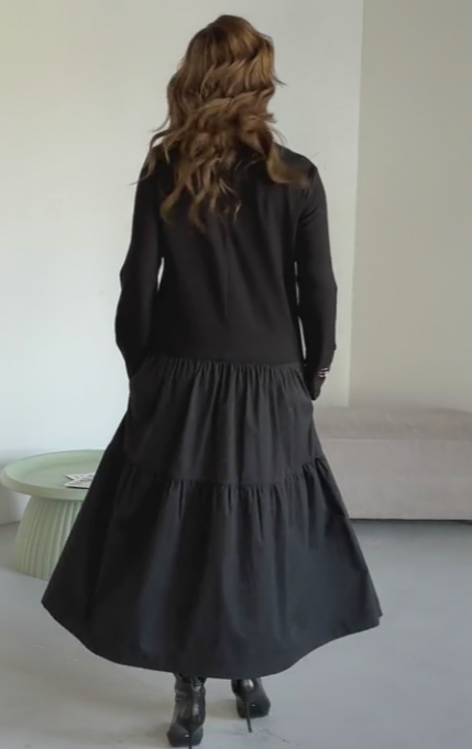 O vestido apresenta um decote com fecho, mangas compridas e uma saia plissada em camadas.