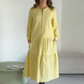 O vestido apresenta um decote com fecho, mangas compridas e uma saia plissada em camadas.