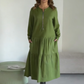 O vestido apresenta um decote com fecho, mangas compridas e uma saia plissada em camadas.