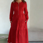 O vestido apresenta um decote com fecho, mangas compridas e uma saia plissada em camadas.