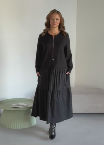 O vestido apresenta um decote com fecho, mangas compridas e uma saia plissada em camadas.