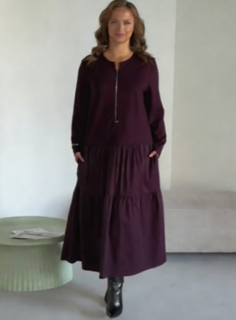 O vestido apresenta um decote com fecho, mangas compridas e uma saia plissada em camadas.