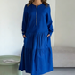 O vestido apresenta um decote com fecho, mangas compridas e uma saia plissada em camadas.