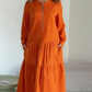 O vestido apresenta um decote com fecho, mangas compridas e uma saia plissada em camadas.