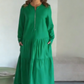 O vestido apresenta um decote com fecho, mangas compridas e uma saia plissada em camadas.